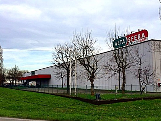 Fotografia di esterni del punto vendita Alta Sfera a Modena, che mostra un ampio edificio commerciale moderno con insegna circolare, circondato da prato e alberi.